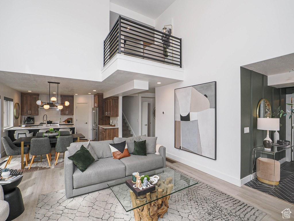 Living room featuring light wood-type flooring, stairway, a towering ceiling, and baseboards