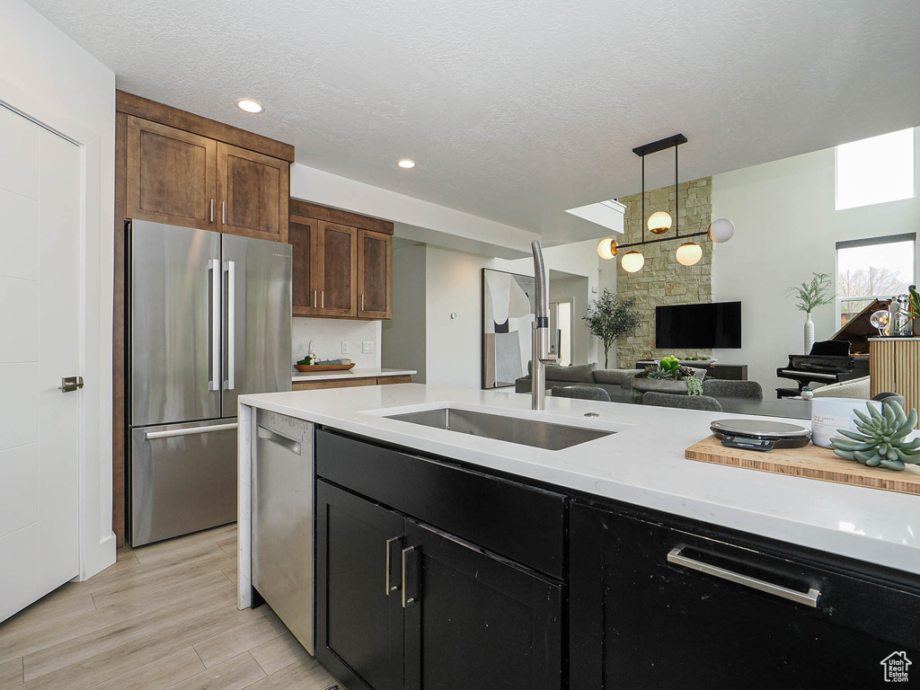 Kitchen with stainless steel appliances, light countertops, open floor plan, decorative light fixtures, and a textured ceiling