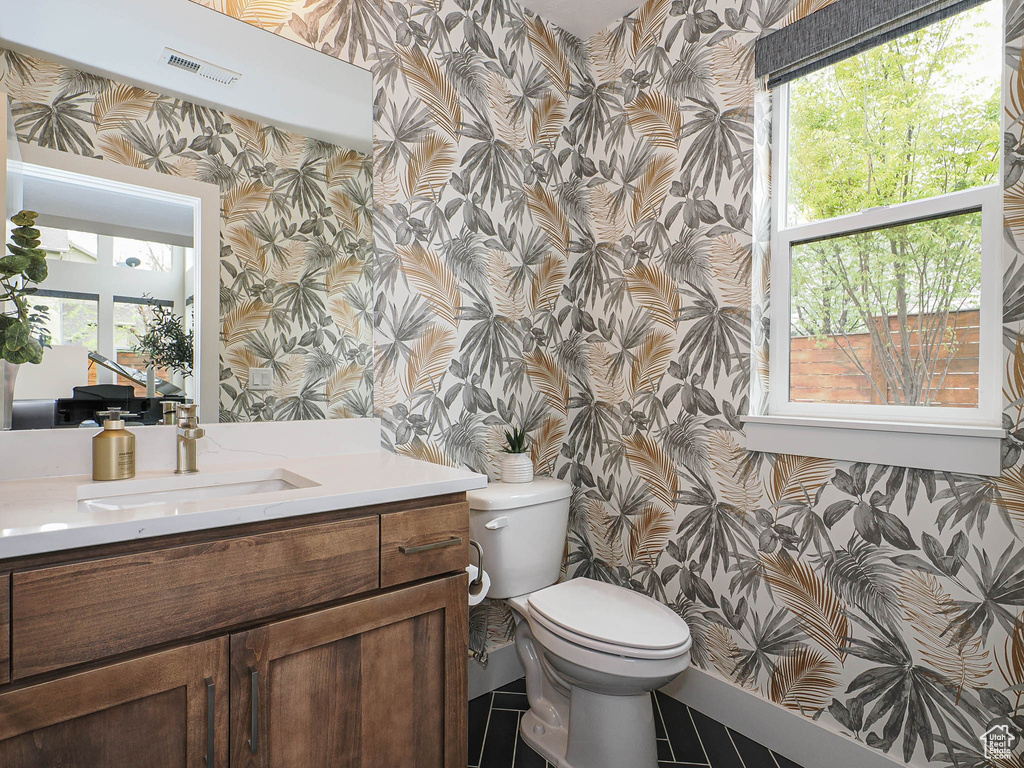 Bathroom featuring wallpapered walls, vanity, toilet, healthy amount of natural light, and baseboards