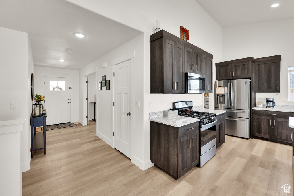 Kitchen with stainless steel appliances, light wood-type flooring, dark brown cabinets, recessed lighting, and light stone countertops