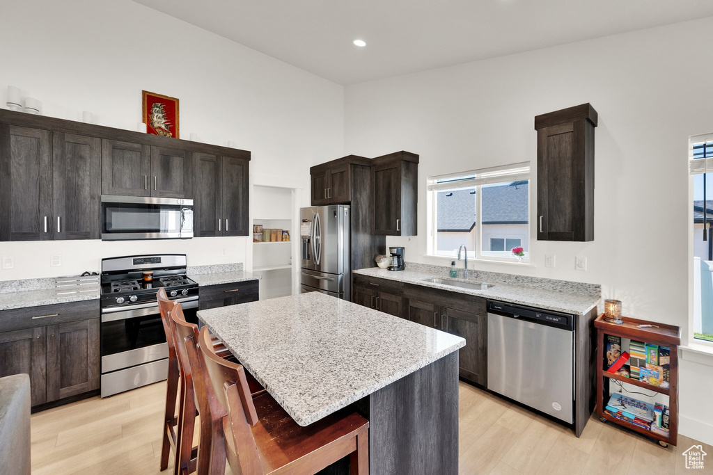 Kitchen with appliances with stainless steel finishes, a sink, light wood finished floors, a kitchen island, and recessed lighting