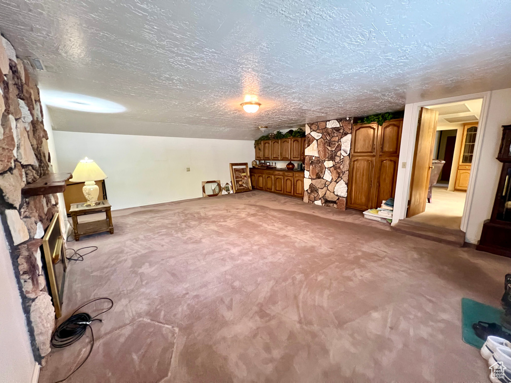 Unfurnished room featuring a textured ceiling, light carpet, and a stone fireplace