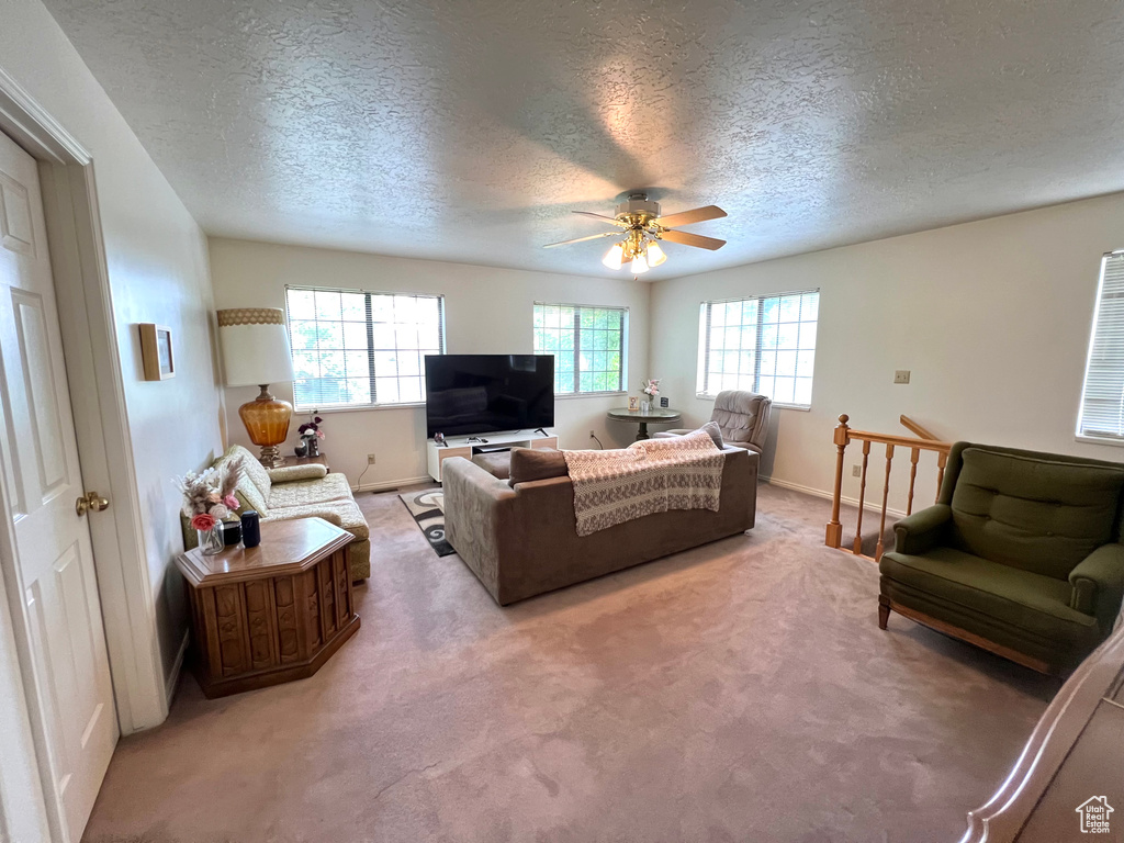 Living area with a textured ceiling, a ceiling fan, light carpet, and baseboards