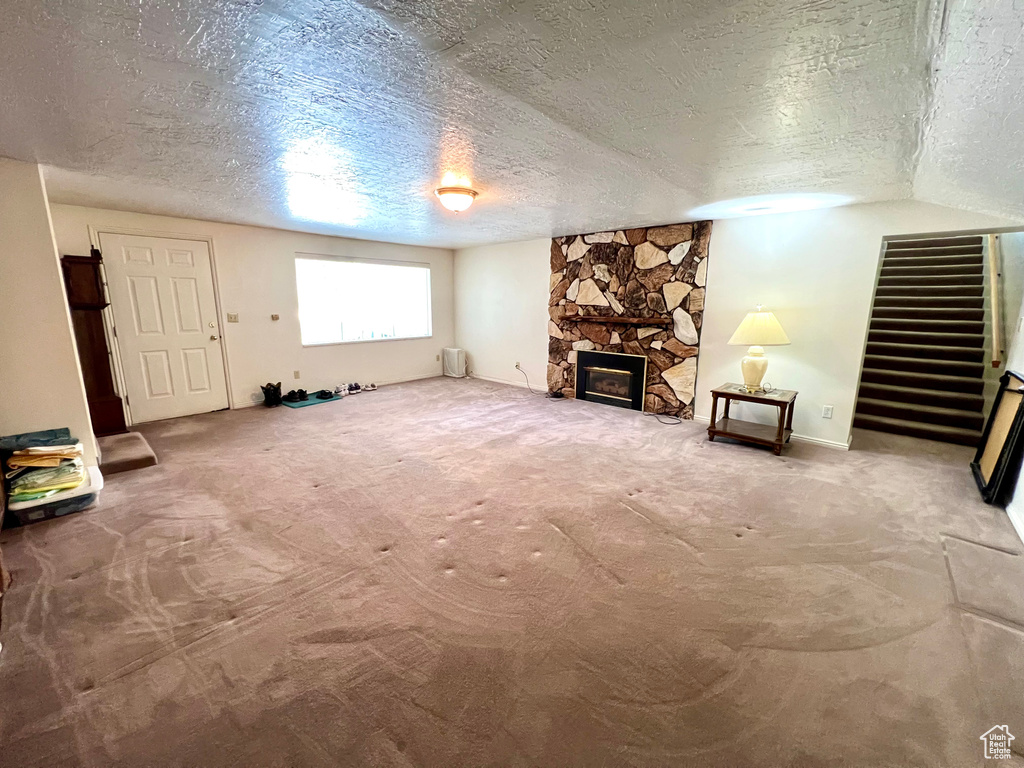 Unfurnished living room featuring a textured ceiling, a fireplace, and carpet floors
