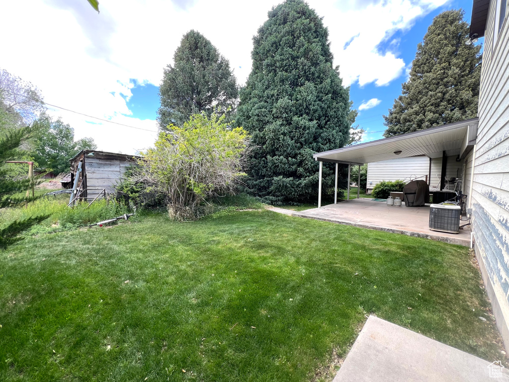View of grassy yard featuring a patio area and central air condition unit