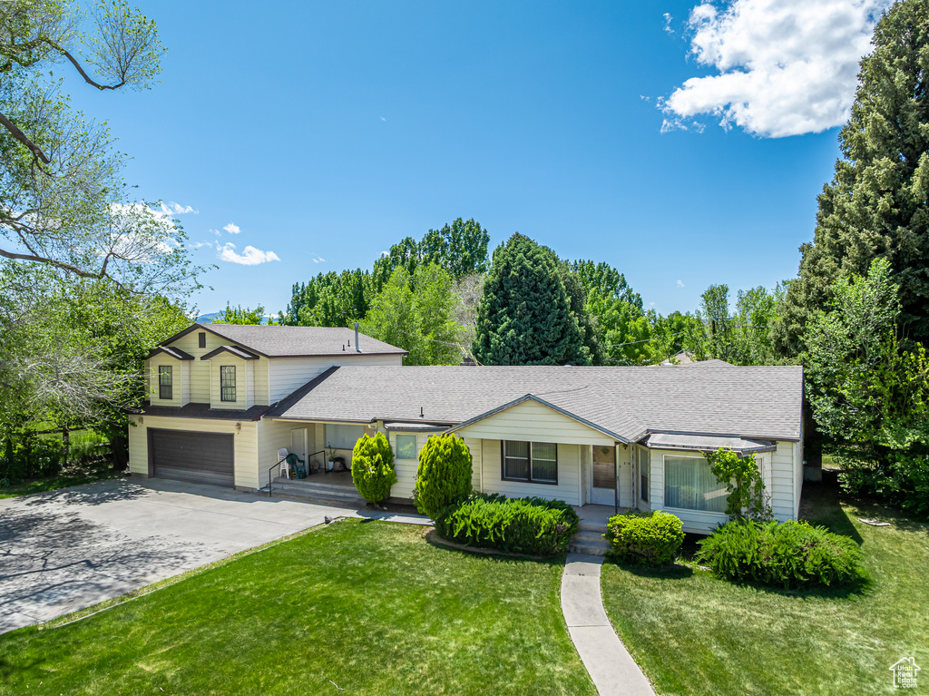 View of front of house with a porch, a front yard, an attached garage, concrete driveway, and a shingled roof