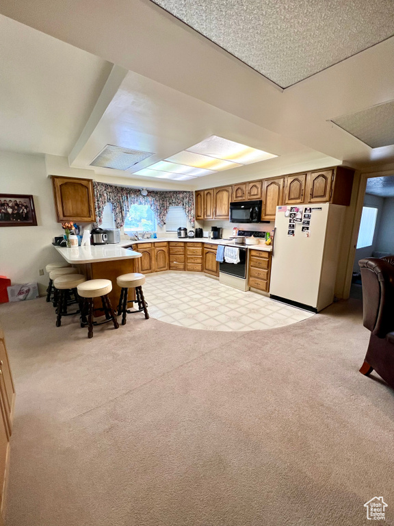 Kitchen featuring white appliances, brown cabinetry, light countertops, light carpet, and a peninsula