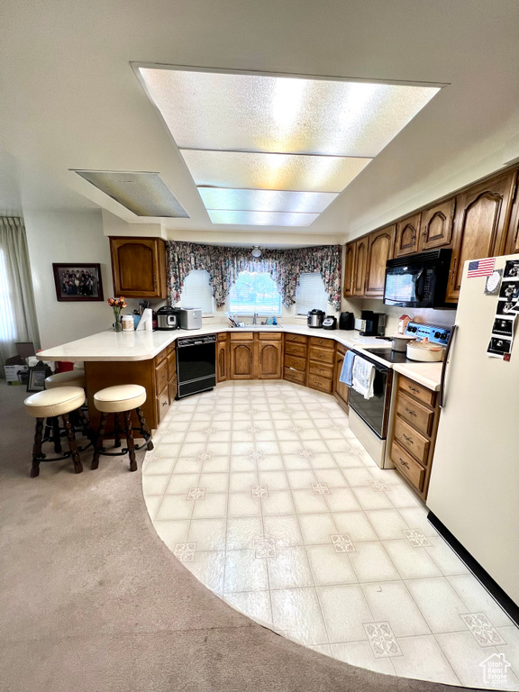 Kitchen with black appliances, a sink, light countertops, brown cabinetry, and a peninsula