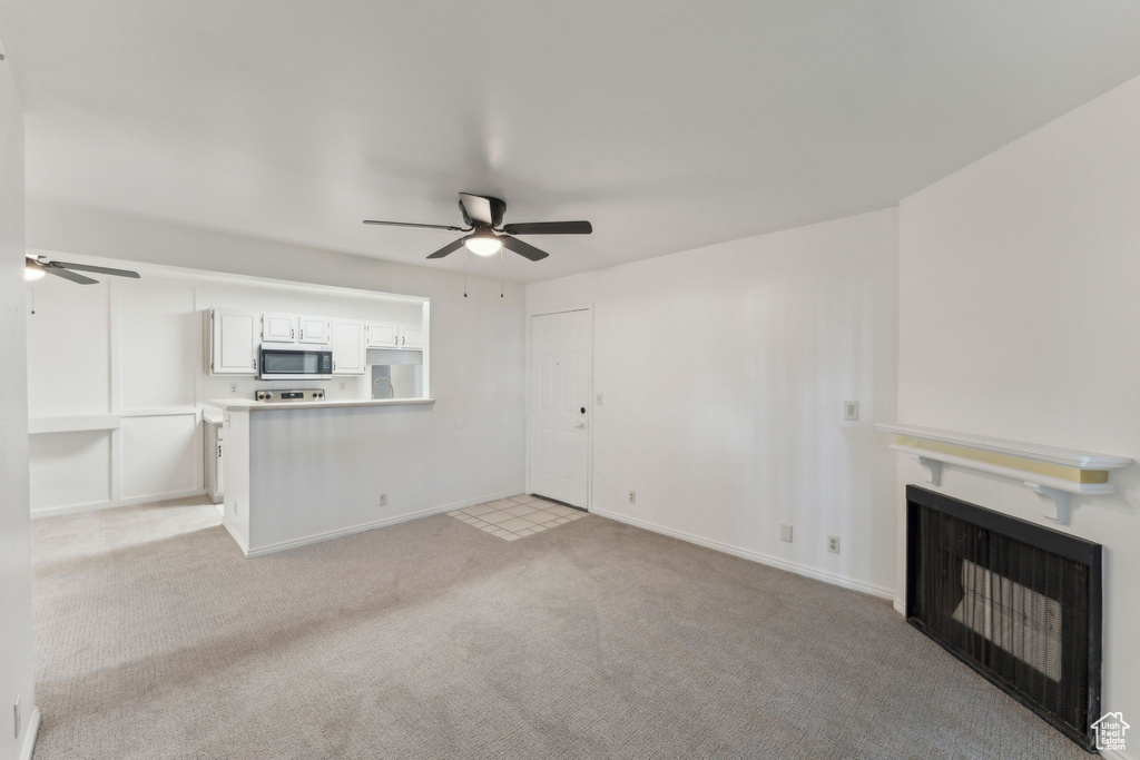 Unfurnished living room featuring a ceiling fan, a fireplace, light carpet, baseboards, and heating unit