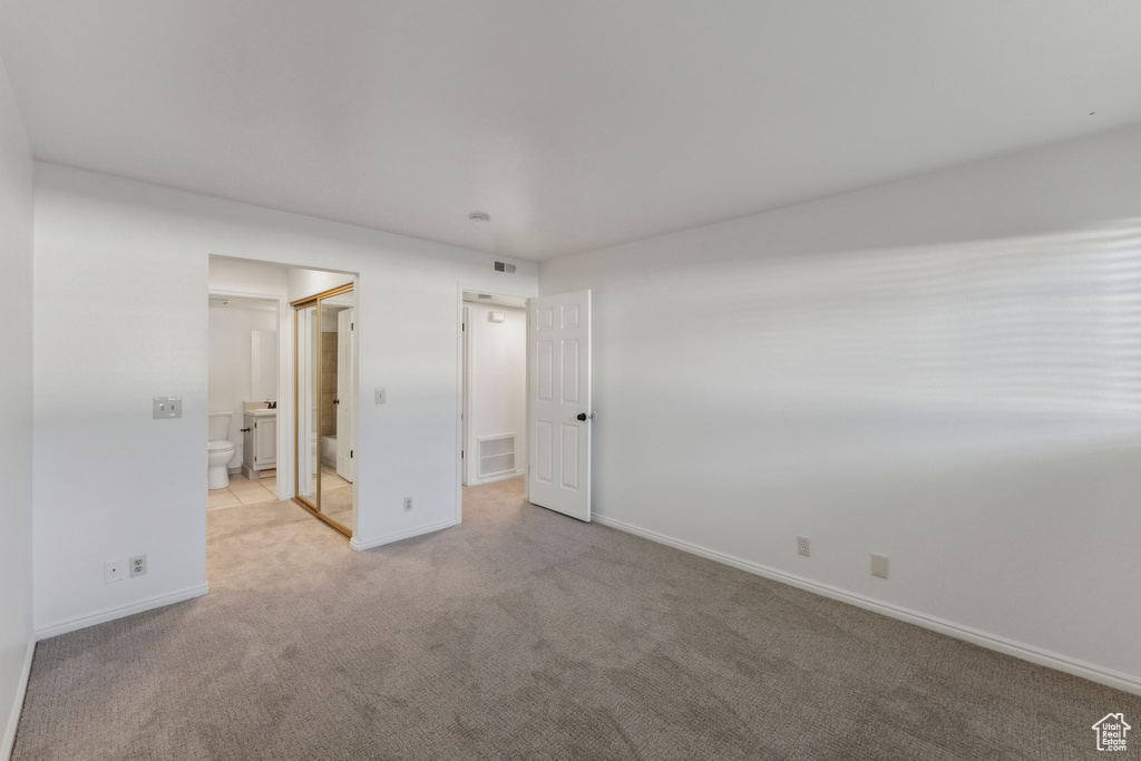 Unfurnished bedroom featuring light carpet, baseboards, ensuite bath, and washer / clothes dryer