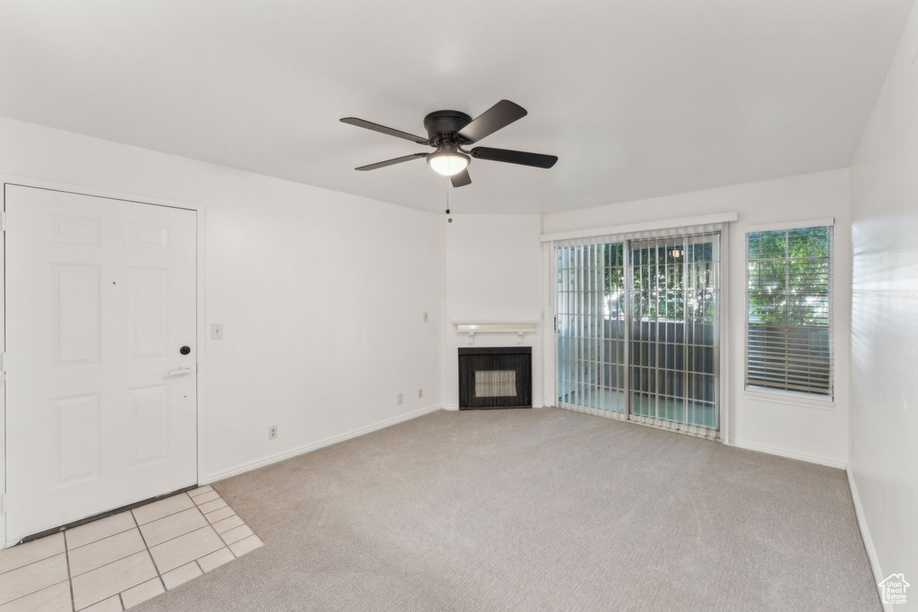 Unfurnished living room featuring a ceiling fan, light carpet, baseboards, and a glass covered fireplace