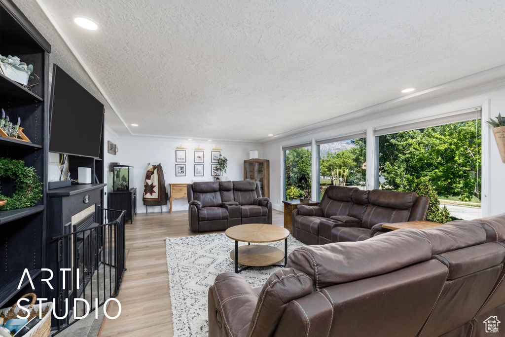 Living area featuring a textured ceiling, recessed lighting, light wood-type flooring, and crown molding