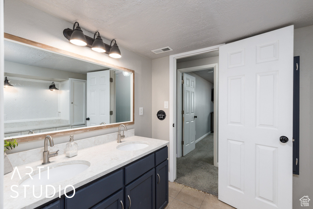Full bath featuring double vanity, tile patterned floors, and a textured ceiling