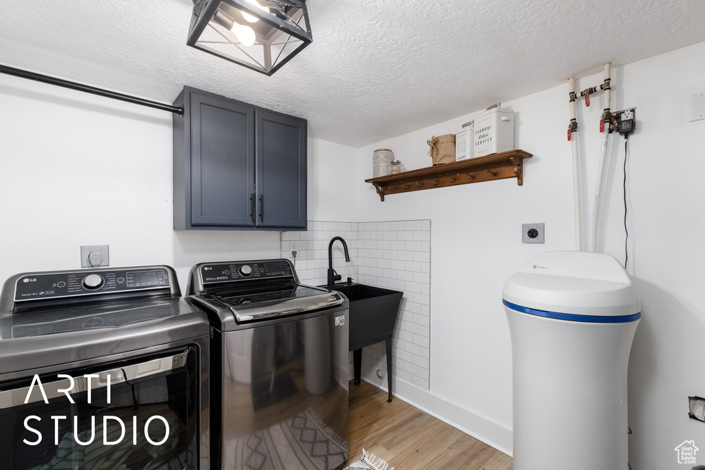 Laundry room with cabinet space, washer and clothes dryer, light wood finished floors, and a textured ceiling