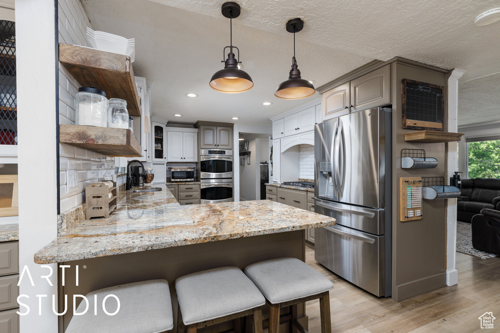 Kitchen featuring appliances with stainless steel finishes, a peninsula, light wood-type flooring, open shelves, and a sink