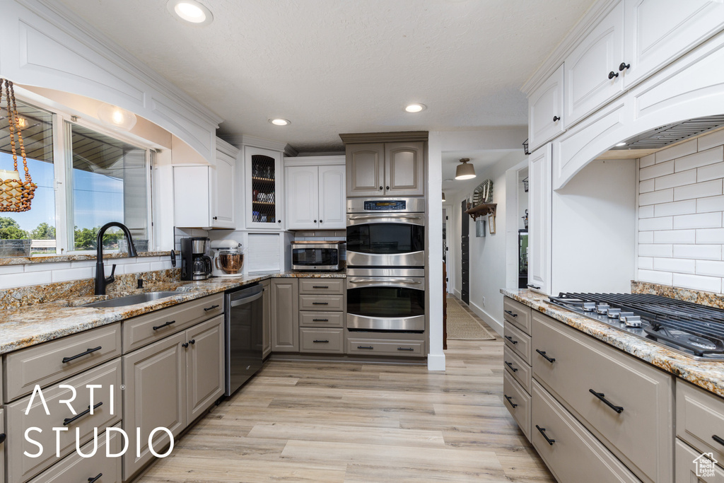 Kitchen with stainless steel appliances, a sink, gray cabinetry, tasteful backsplash, and light wood-style floors