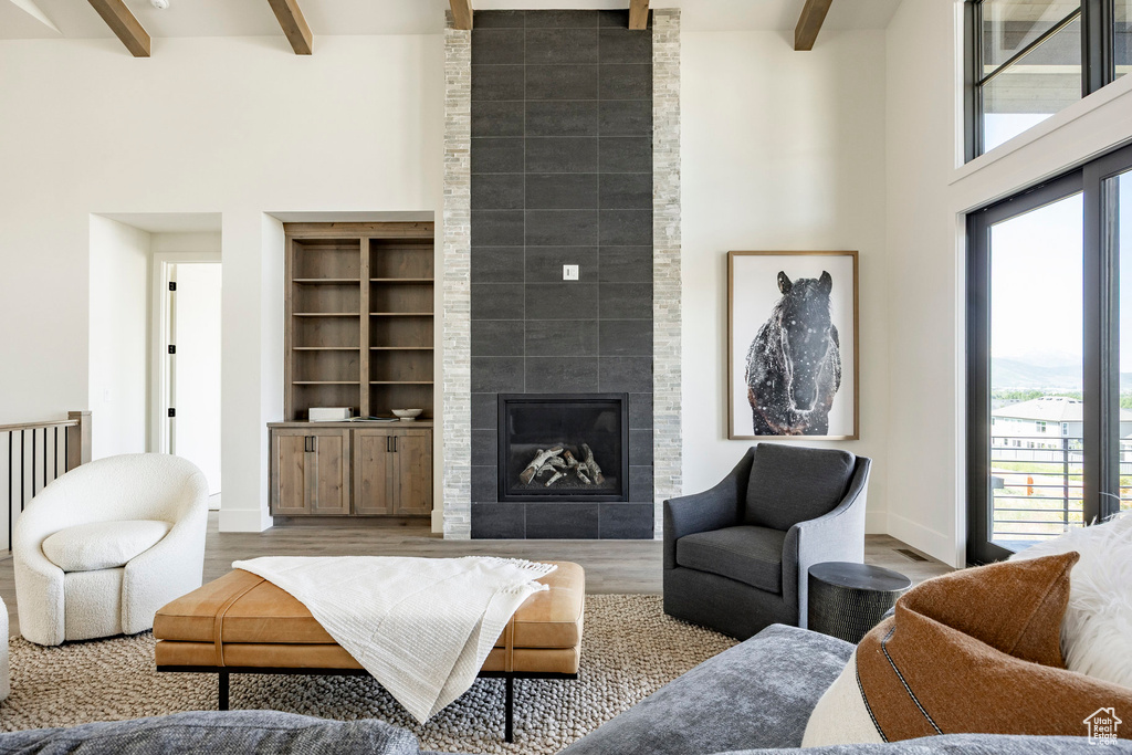Living room with beam ceiling, a fireplace, wood finished floors, a high ceiling, and baseboards