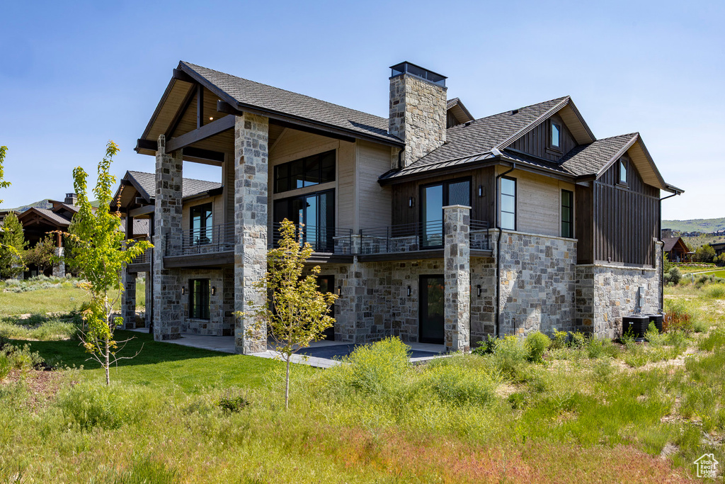 Back of house with stone siding, a balcony, a chimney, a standing seam roof, and board and batten siding
