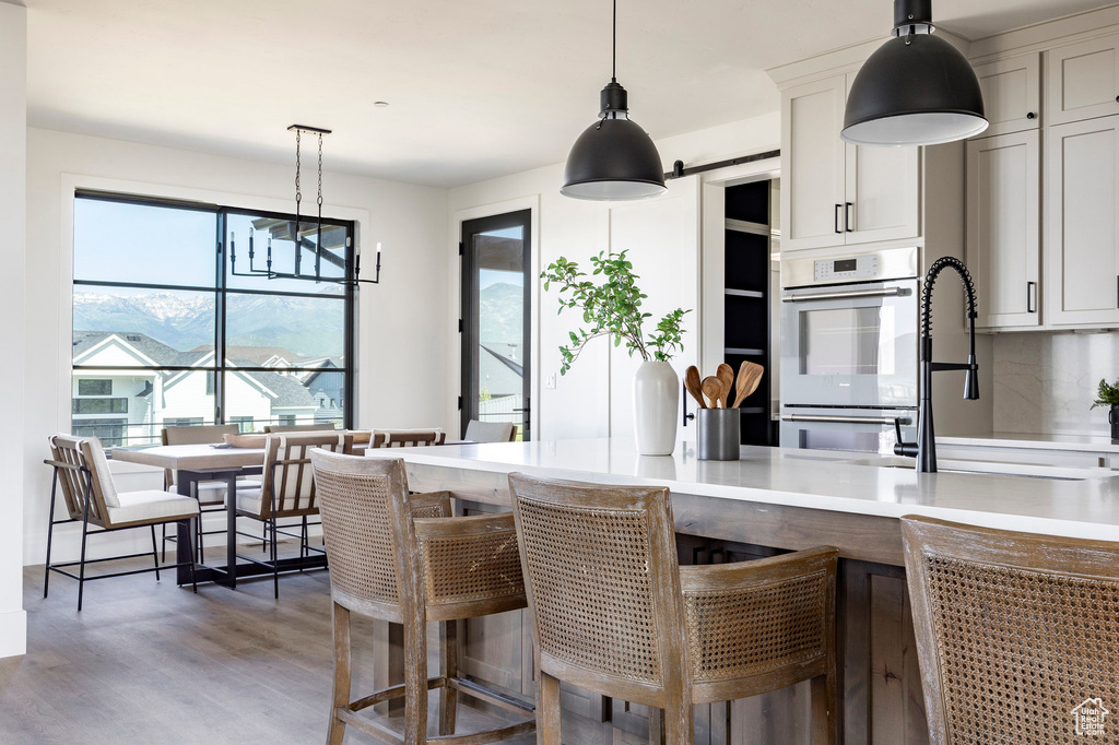 Kitchen featuring light wood-type flooring, light countertops, pendant lighting, double wall oven, and a breakfast bar