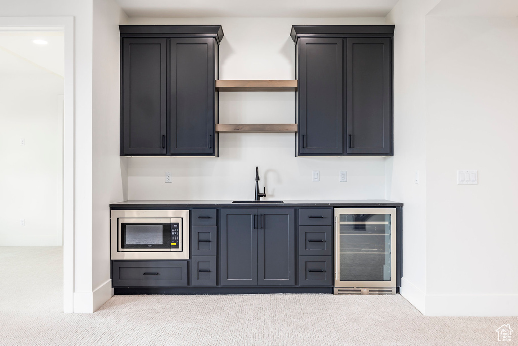 Bar featuring wine cooler, a sink, carpet flooring, and stainless steel microwave
