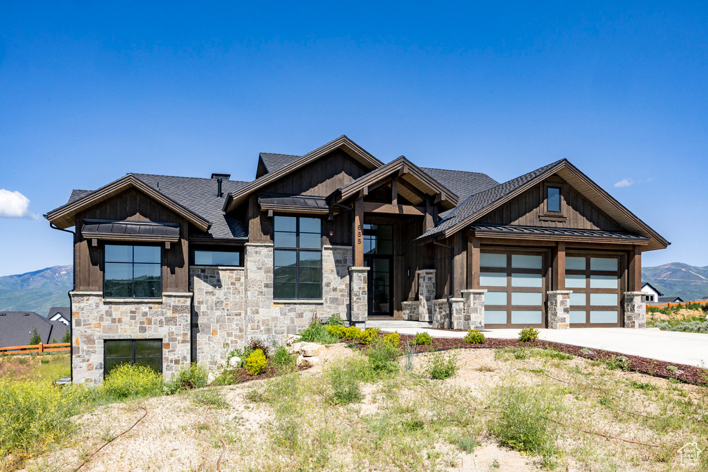 View of front facade featuring board and batten siding, stone siding, a standing seam roof, concrete driveway, and roof with shingles