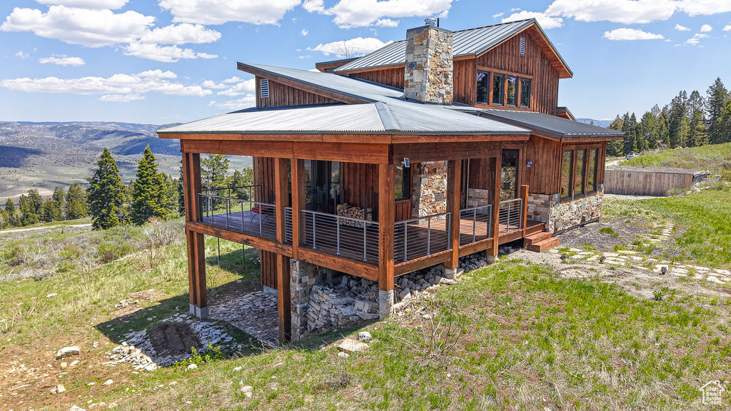 Rear view of property with stone siding, a standing seam roof, metal roof, a chimney, and a deck with mountain view