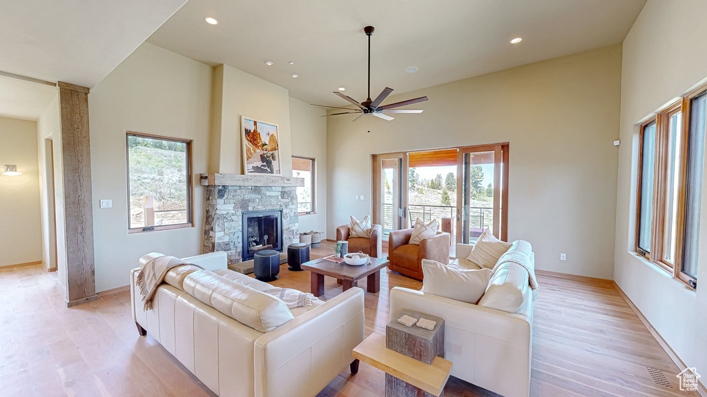 Living room with a towering ceiling, light wood-type flooring, a fireplace, recessed lighting, and a ceiling fan