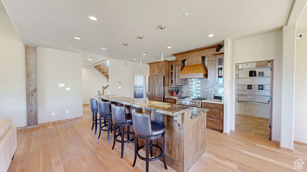 Kitchen with custom range hood, light wood-type flooring, a large island, a breakfast bar area, and brown cabinetry