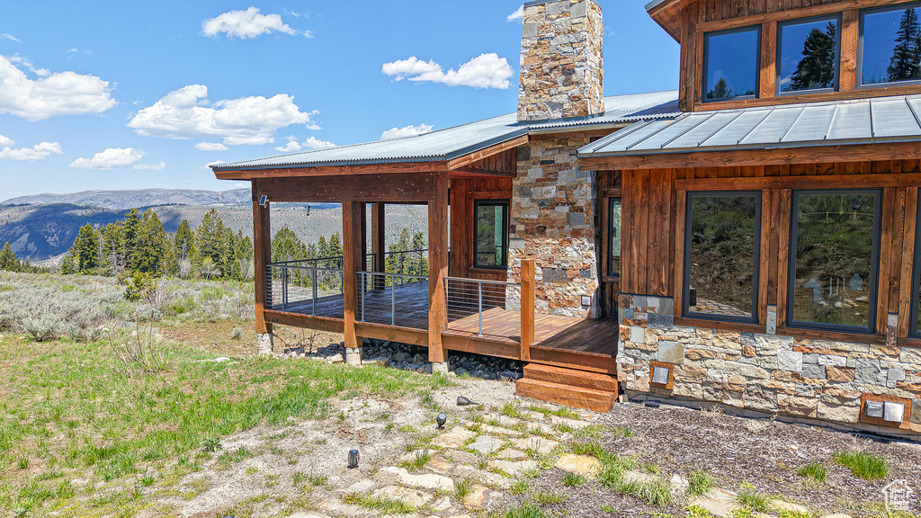 View of exterior entry with a deck with mountain view, a chimney, stone siding, and metal roof
