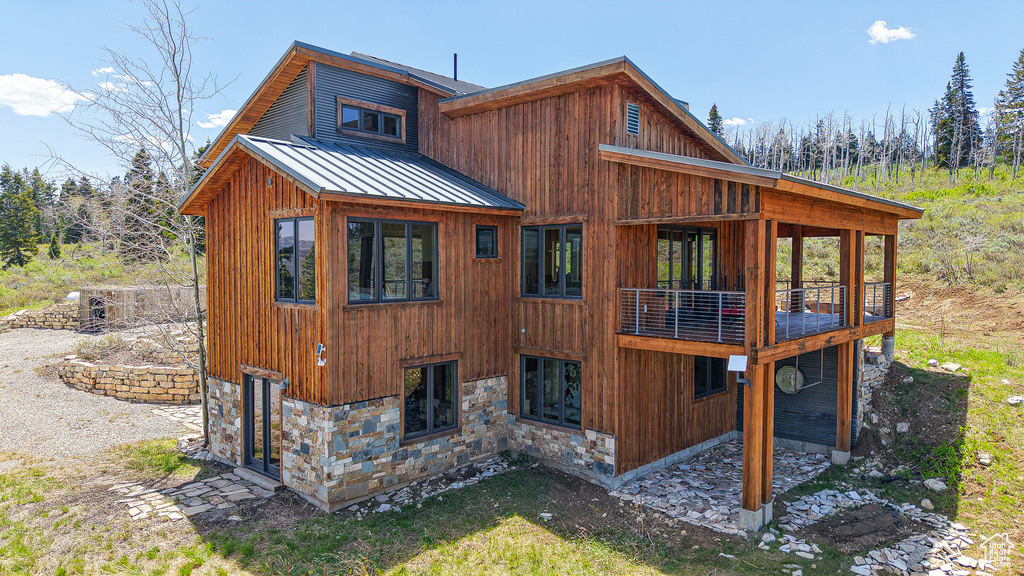 Back of property featuring a standing seam roof, stone siding, and metal roof