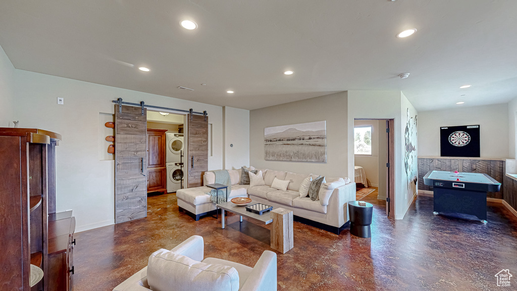 Living room featuring stacked washer / drying machine, finished concrete floors, a barn door, recessed lighting, and baseboards