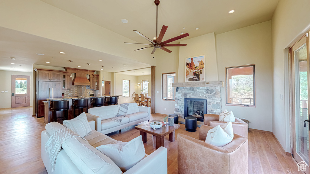 Living room featuring light wood-style flooring, a ceiling fan, recessed lighting, a stone fireplace, and a towering ceiling