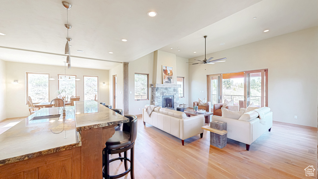Living area with light wood-type flooring, healthy amount of natural light, a stone fireplace, recessed lighting, and ceiling fan