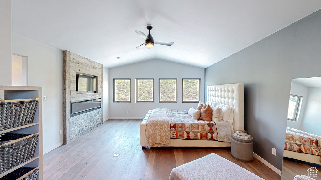 Bedroom with multiple windows, a fireplace, vaulted ceiling, wood finished floors, and ceiling fan