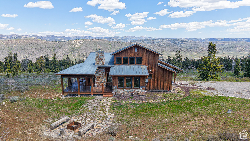Rustic home featuring a chimney, metal roof, a deck with mountain view, stone siding, and a standing seam roof