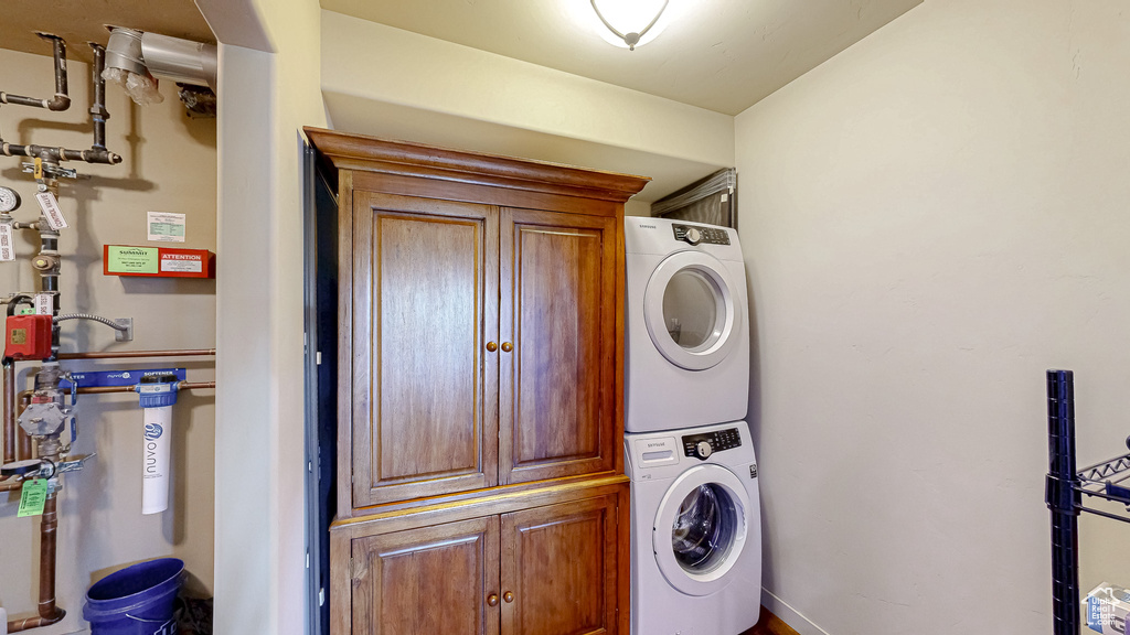 Washroom featuring stacked washer / drying machine, cabinet space, and baseboards