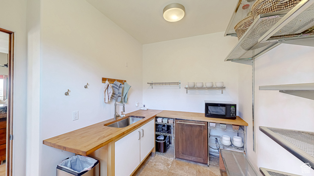 Kitchen featuring black microwave, wooden counters, white cabinetry, light stone finish floors, and custom range hood