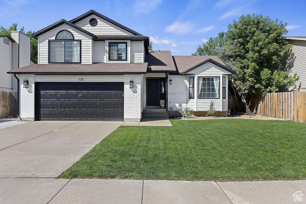 Traditional home featuring a garage, driveway, brick siding, and a shingled roof