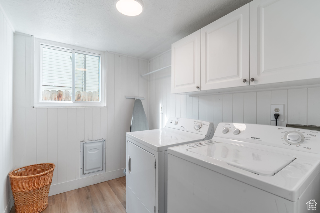 Laundry area featuring washing machine and clothes dryer, cabinet space, and light wood-type flooring