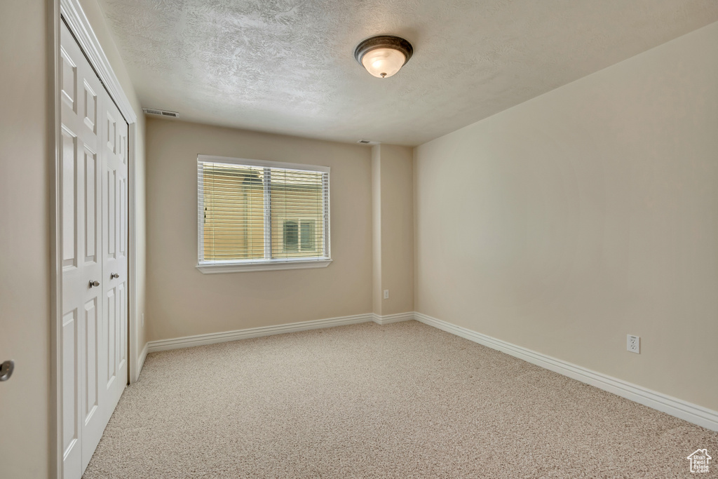 Unfurnished bedroom featuring a textured ceiling, a closet, carpet, and baseboards