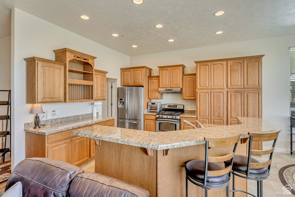 Kitchen featuring stainless steel appliances, recessed lighting, under cabinet range hood, a breakfast bar, and open shelves