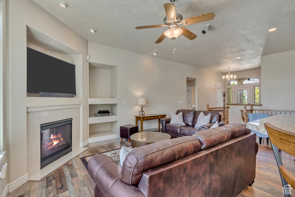 Living area with built in features, a fireplace, ceiling fan, wood finished floors, and recessed lighting