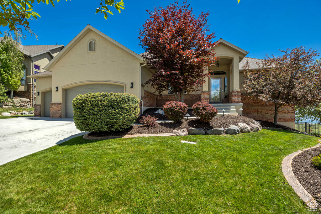 View of property hidden behind natural elements with an attached garage, brick siding, concrete driveway, and stucco siding