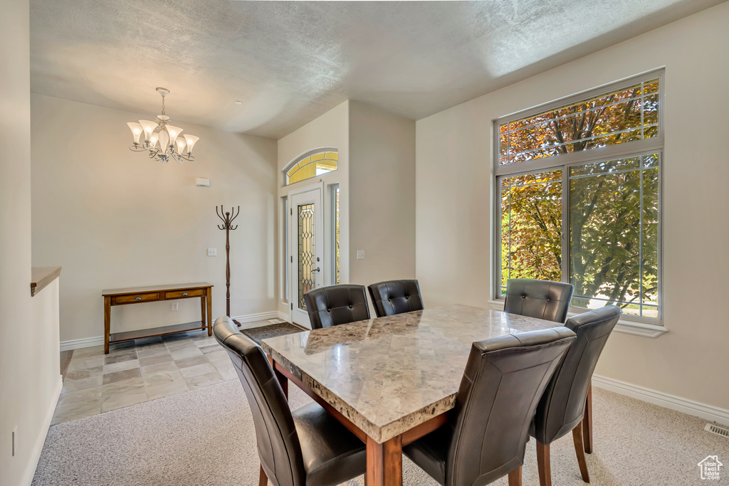 Dining room with a chandelier, baseboards, a textured ceiling, and light colored carpet