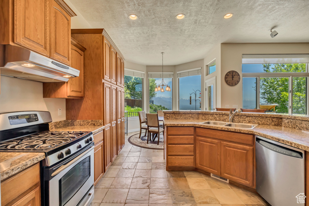 Kitchen featuring stainless steel appliances, under cabinet range hood, a sink, a chandelier, and stone tile flooring