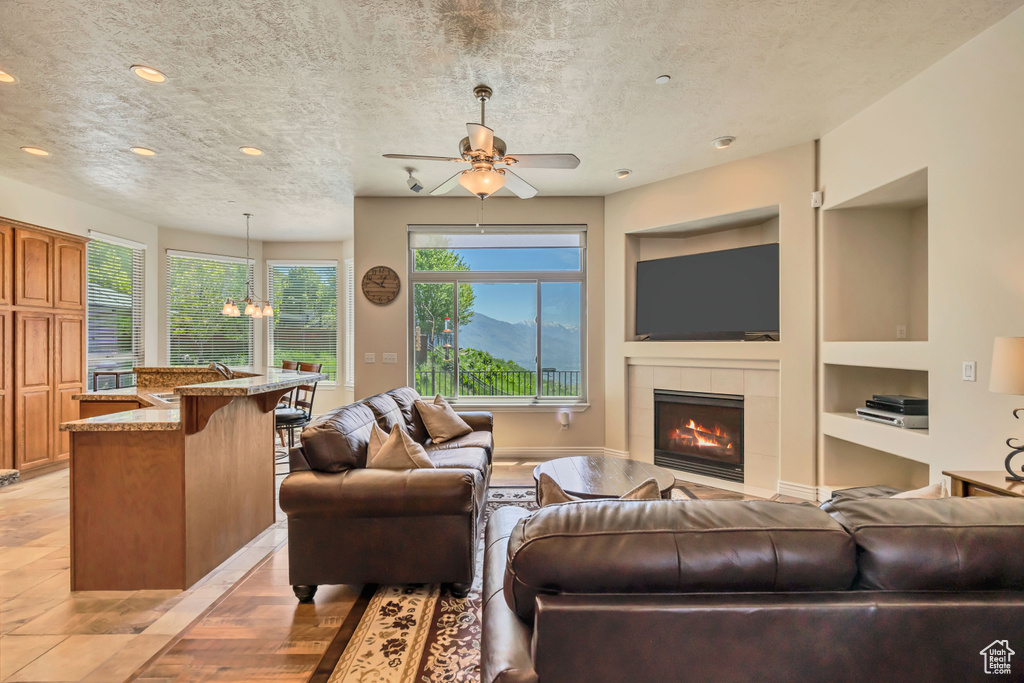Living room featuring built in shelves, a textured ceiling, a tile fireplace, recessed lighting, and a ceiling fan