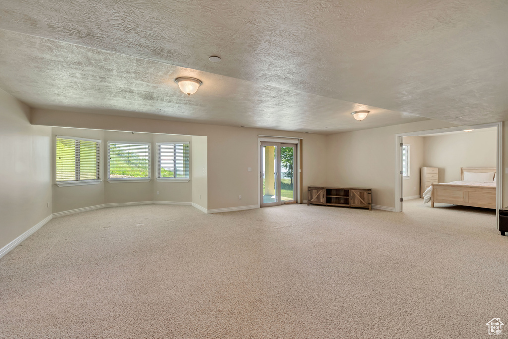 Unfurnished living room with baseboards, a textured ceiling, healthy amount of natural light, and carpet floors