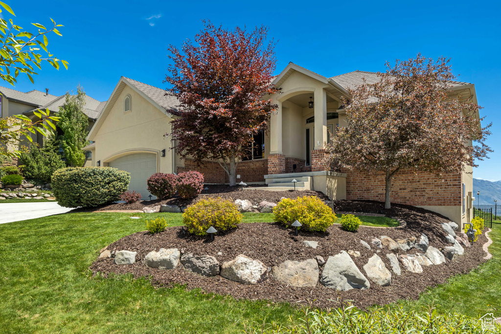 View of property hidden behind natural elements featuring brick siding, an attached garage, stucco siding, and a front lawn