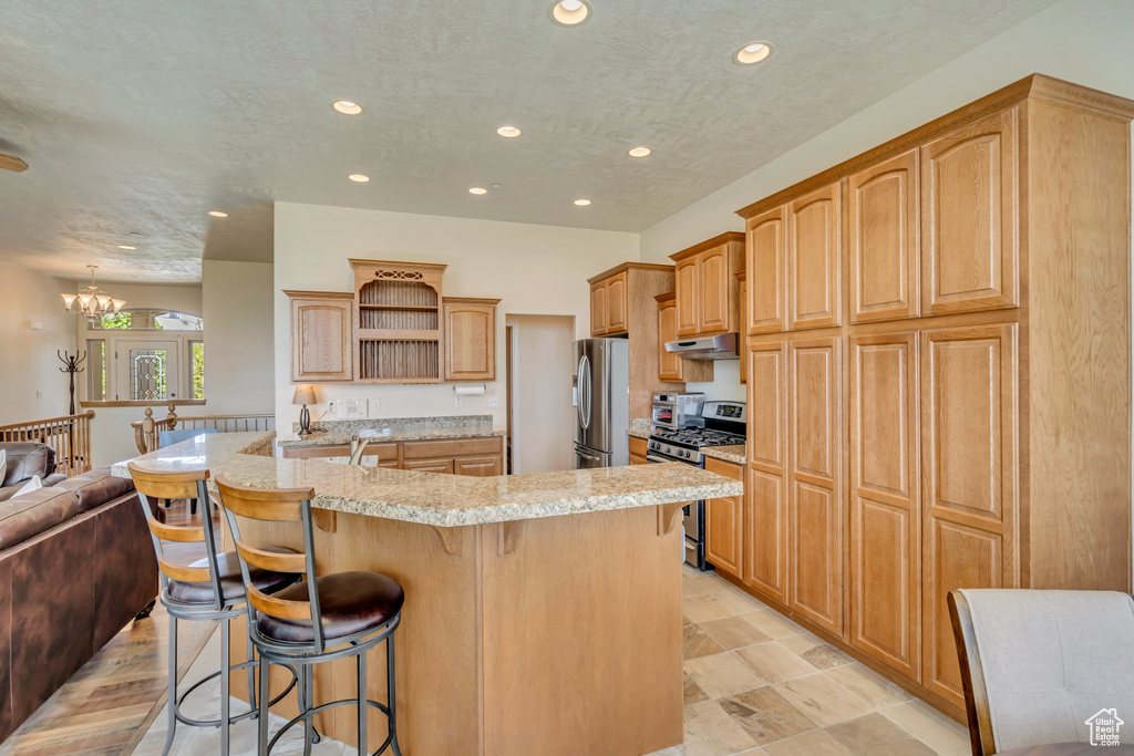 Kitchen with stainless steel appliances, open shelves, under cabinet range hood, a breakfast bar, and recessed lighting