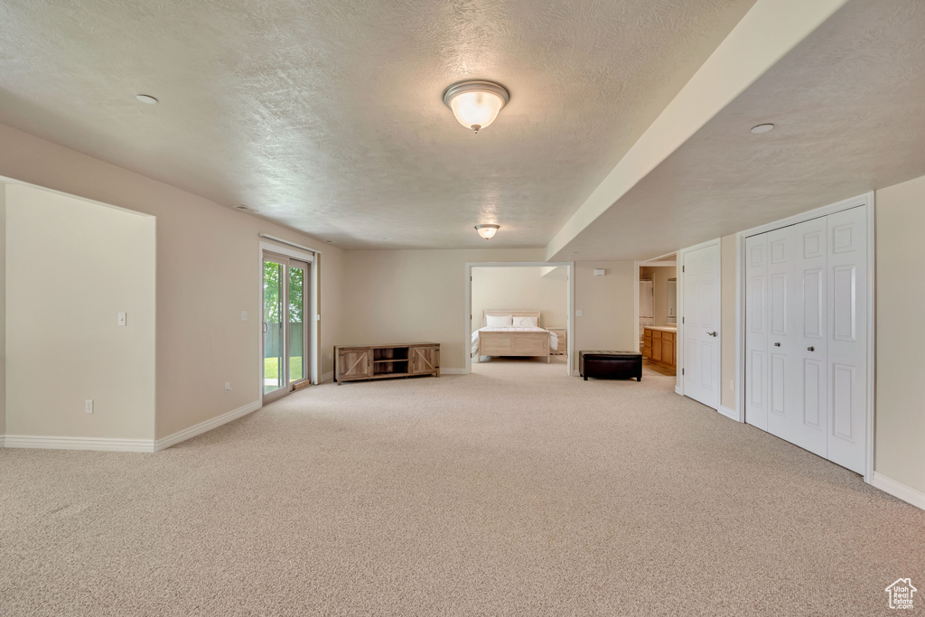 Unfurnished living room with light carpet, baseboards, and a textured ceiling